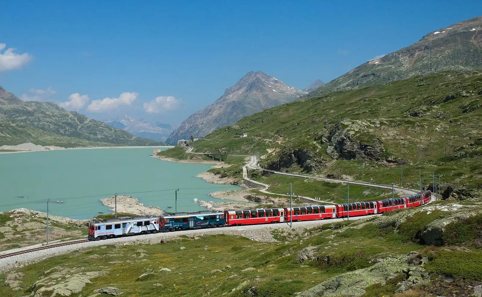 Red Bernina Express train running along the shore of Lago Bianco below alpine peaks