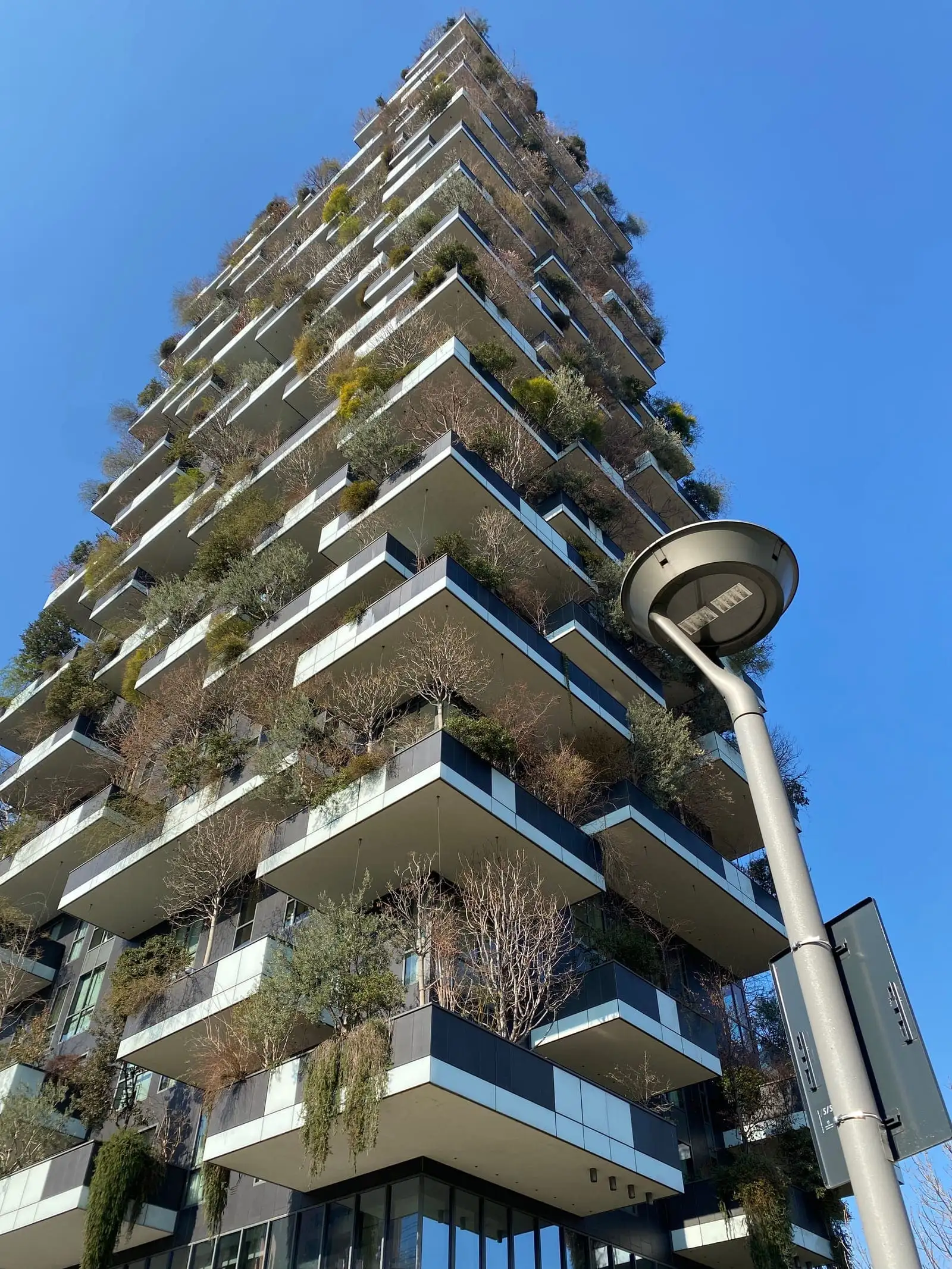 A Bosco Verticale tower with trees growing on every balcony, against a blue sky
