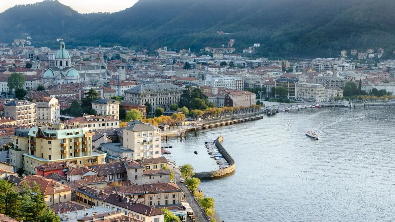 Como town and its lakefront seen from above, with boats in the harbour and mountains behind