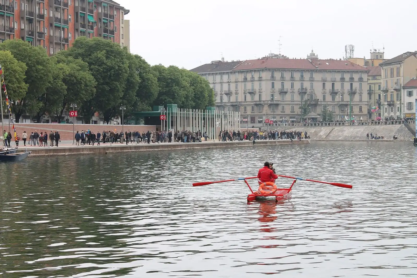 The Darsena dock in Milan after the 2015 renovation, with a red rowing boat on the water and the green covered market on the far bank