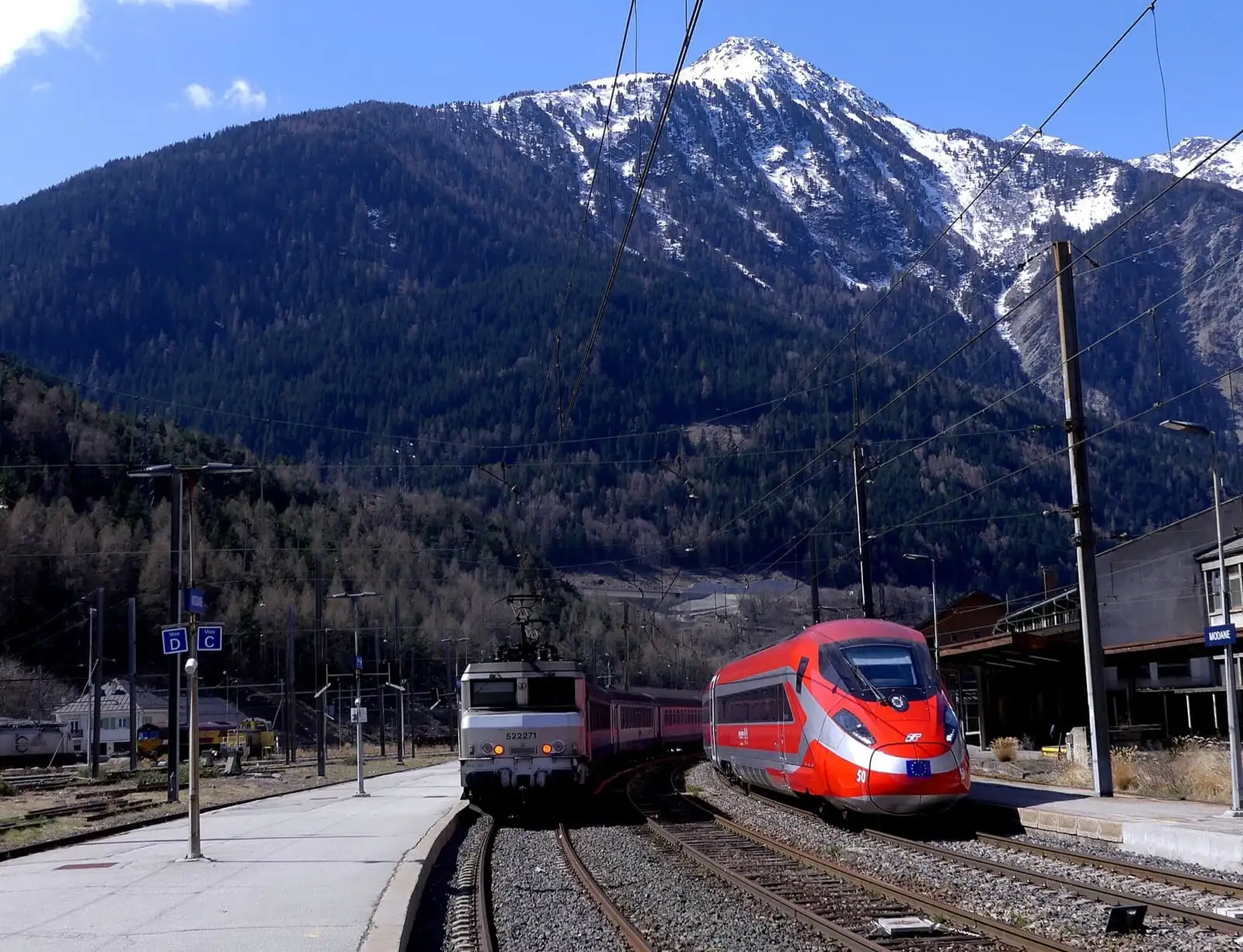 A red Frecciarossa train bound for Milan at Modane station, with snow-capped Alpine peaks behind
