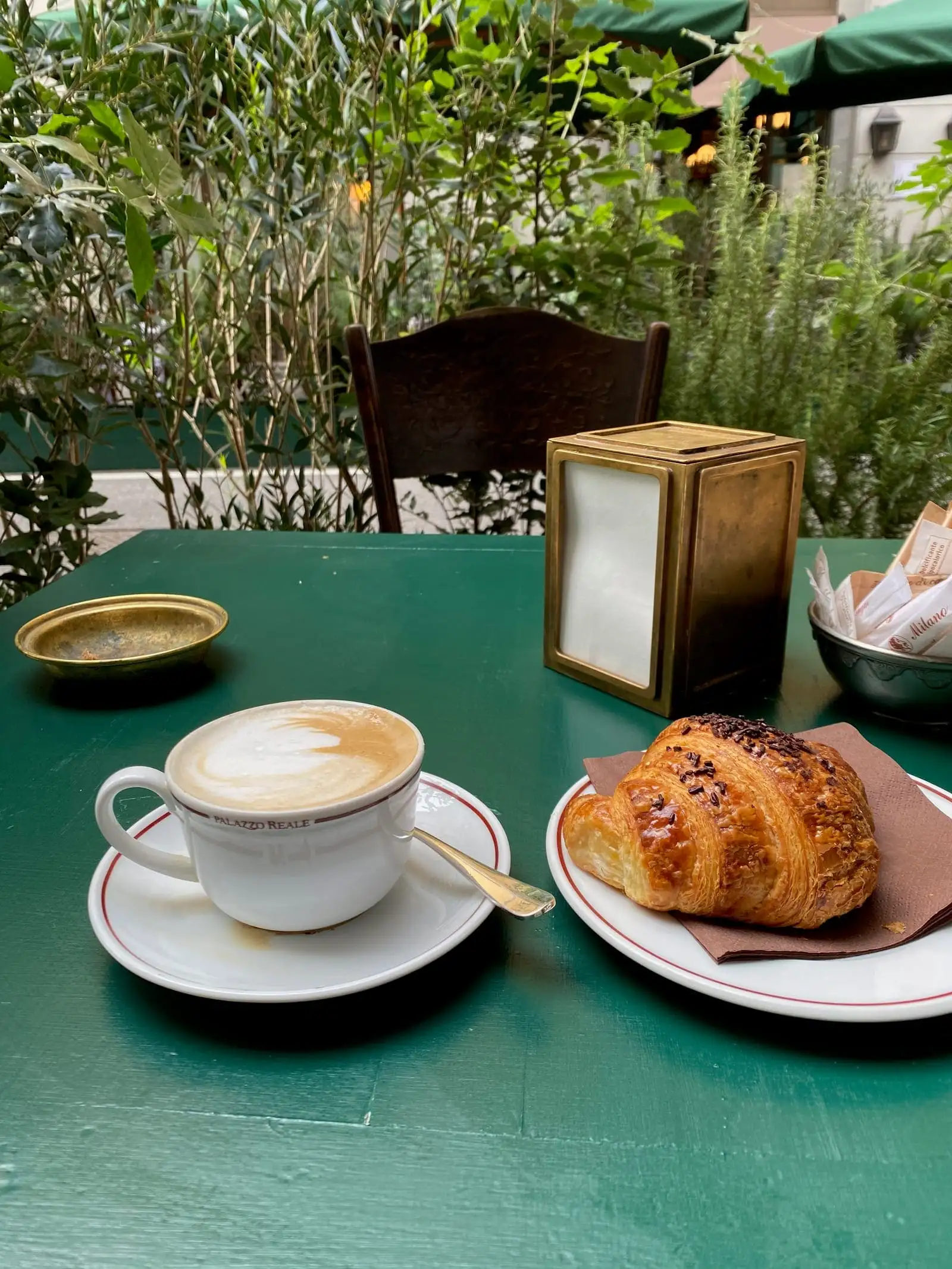 A cappuccino and a brioche on a green café table