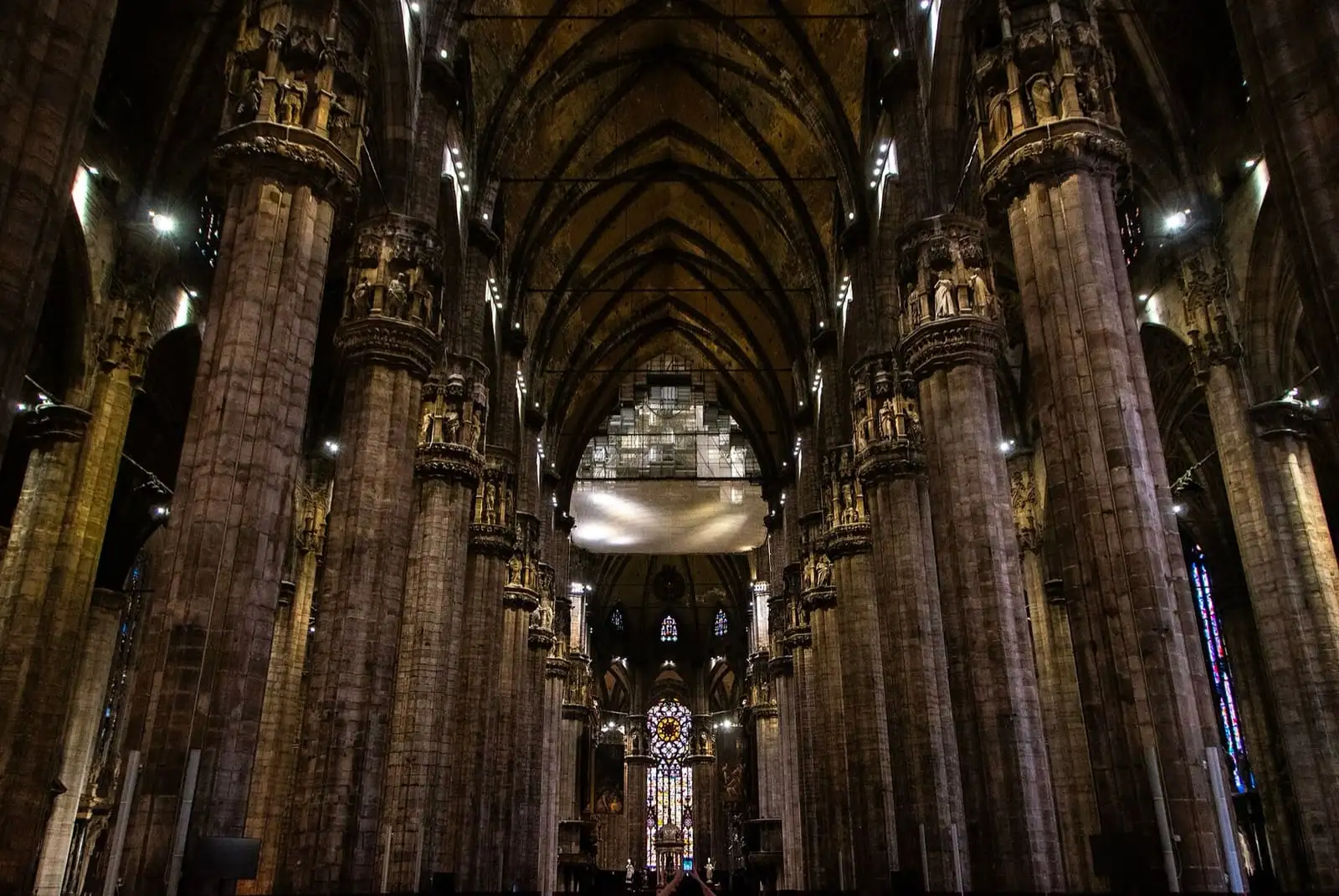 Tall stone columns along the nave of Milan Cathedral, looking toward the altar