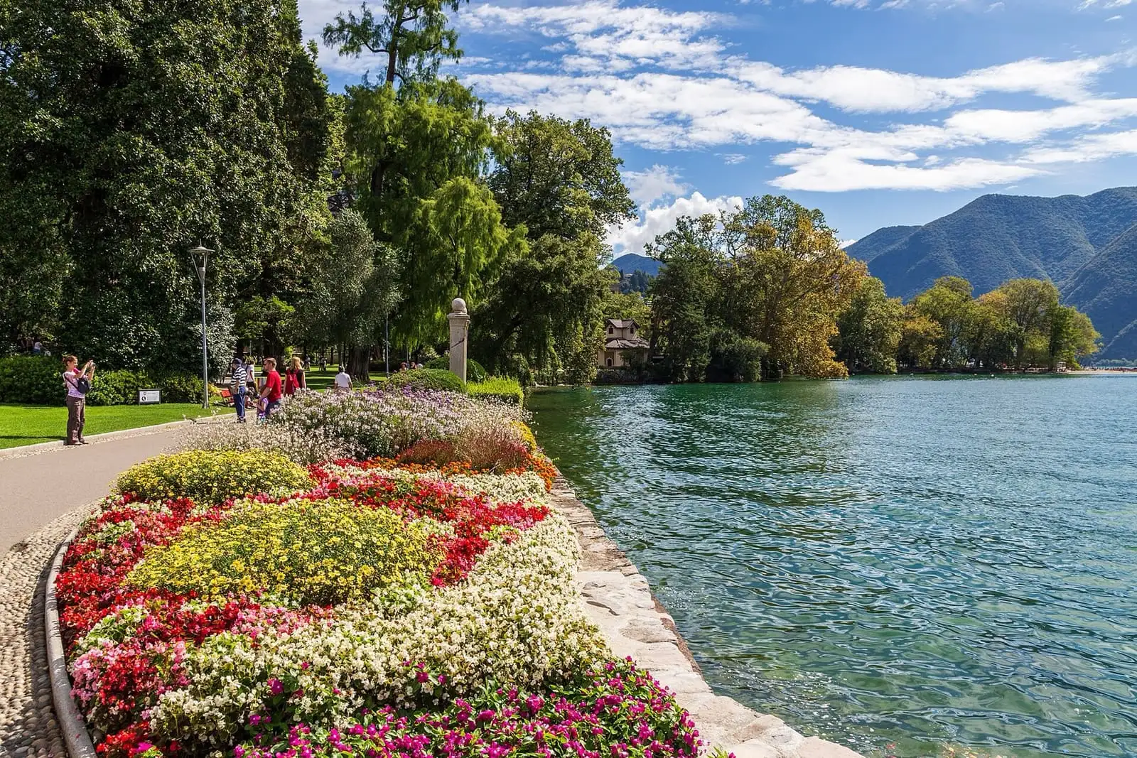 Flower beds and a lakeside path in Parco Ciani, with Lake Lugano and mountains