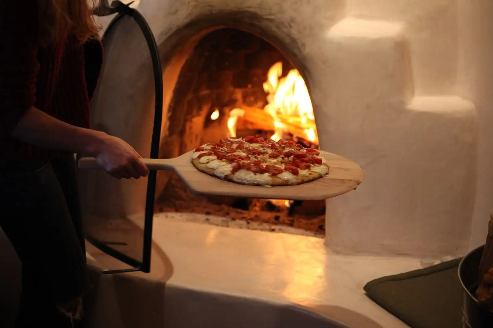 Pizza su una pala di legno davanti a un forno a legna acceso