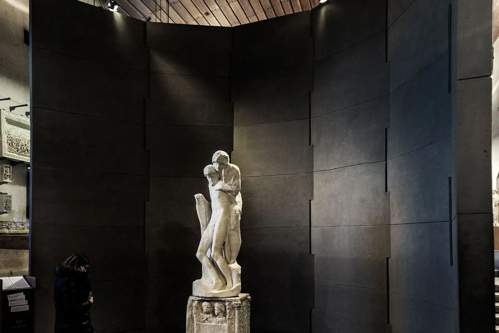 Michelangelo's Rondanini Pietà, a marble statue on a Roman altar base, in a dark curved display