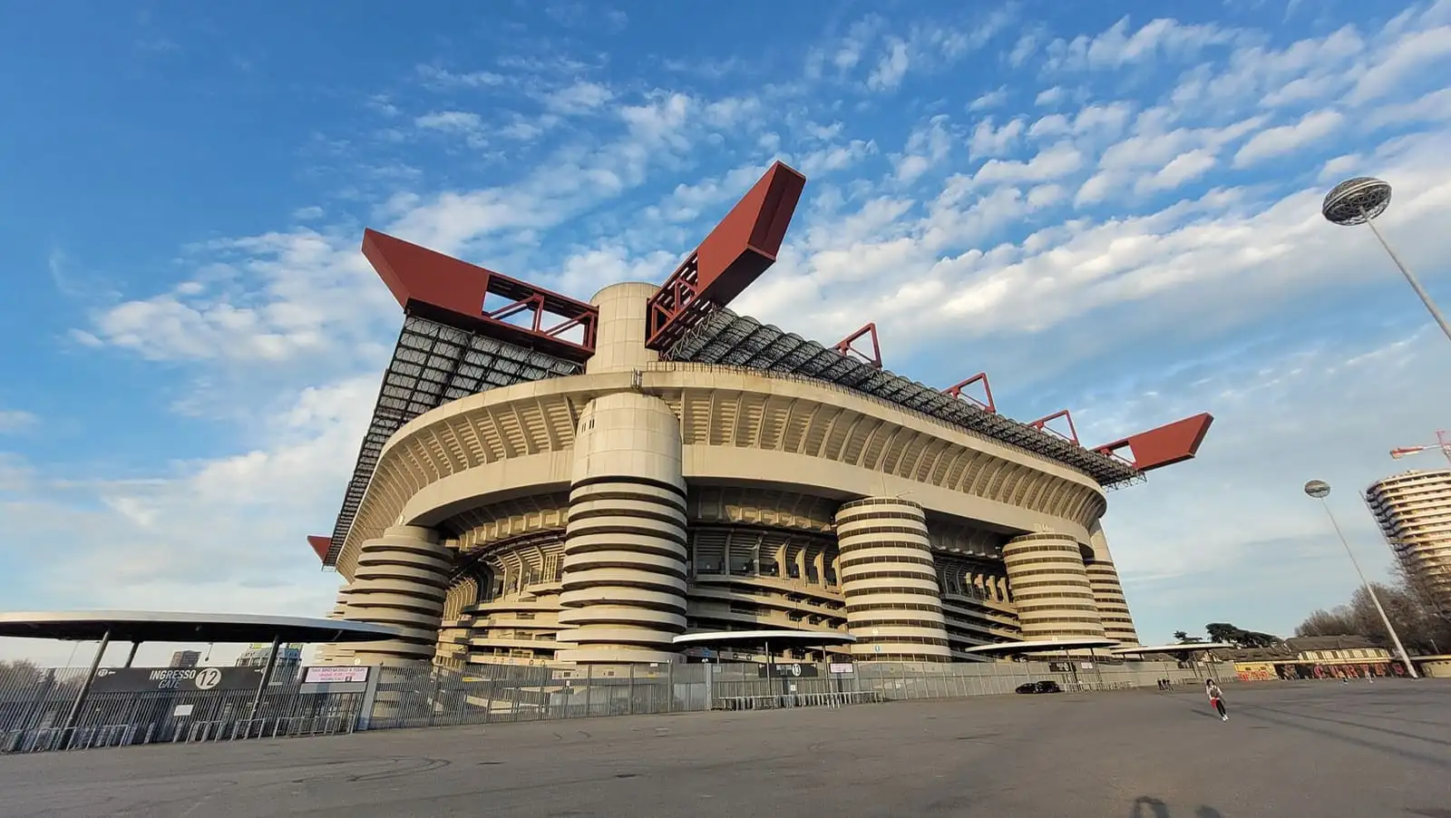 San Siro stadium in Milan with its spiral ramp towers and red roof trusses under a blue sky