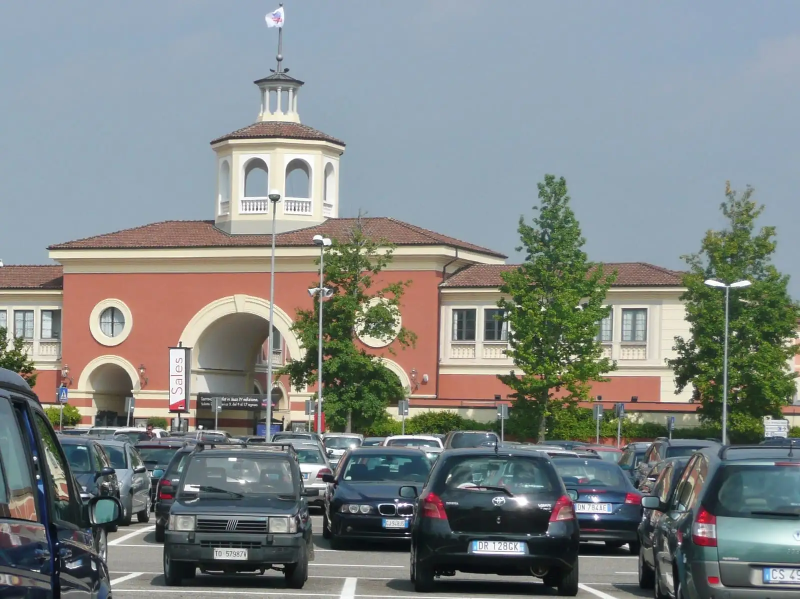 The entrance building of the Serravalle Designer Outlet with its tower, seen across the car park