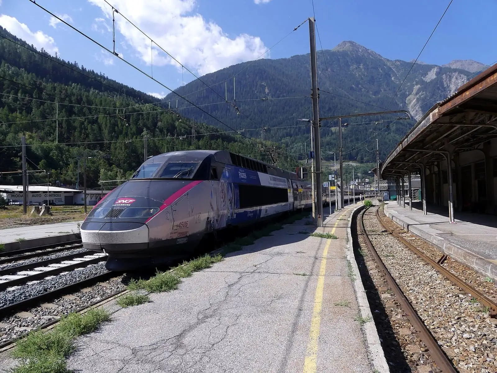 A TGV INOUI train at Modane station in the French Alps, with wooded mountains behind