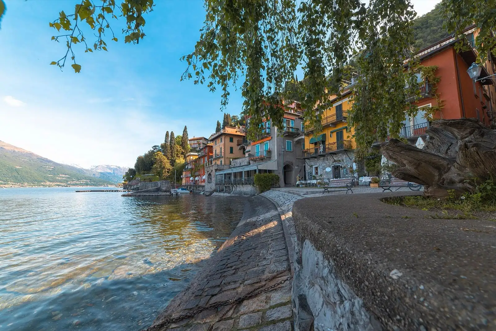 Stone lakeside path in Varenna beside colored houses, with clear water of Lake Como on the left