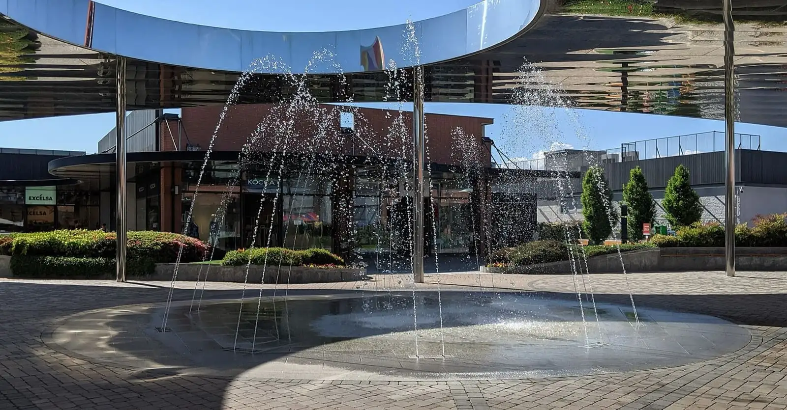Water jets of a fountain under a curved mirrored canopy in the square of Vicolungo The Style Outlets