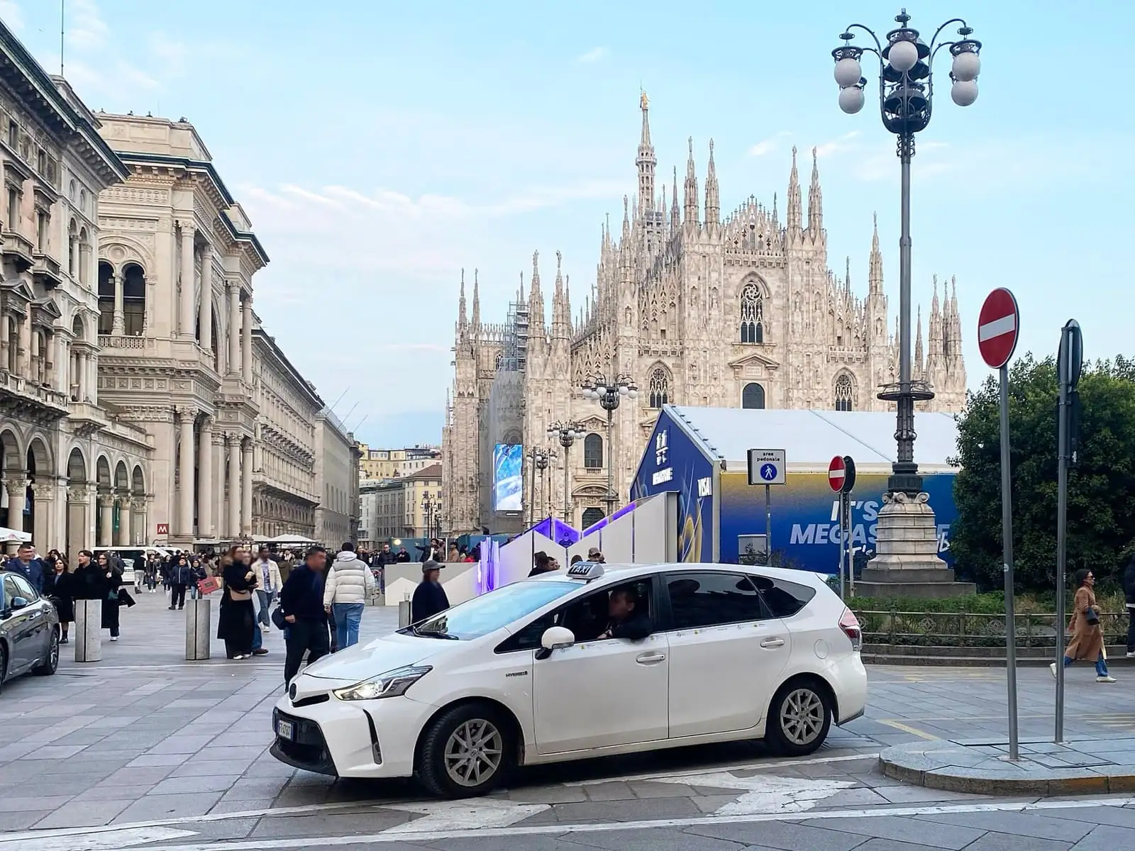 A white licensed Milan taxi with a TAXI roof sign in Piazza del Duomo, with the cathedral behind